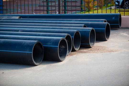 Stack of new black HDPE plastic pipes with blue stripes for cold water supply. Industrial construction site and municipal infrastructure background