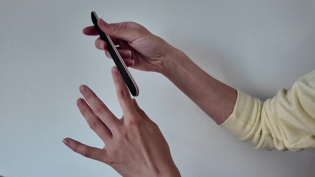 Woman doing manicure at home and filing her nails. Close-up of girl shaping fingernails with nail file during home beauty routine. Self-care, nail care