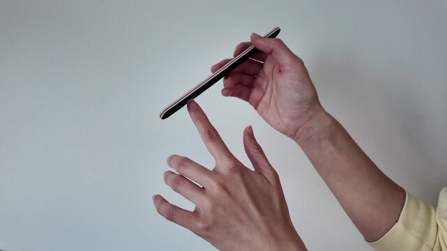 Woman doing manicure at home and filing her nails. Close-up of girl shaping fingernails with nail file during home beauty routine. Self-care, nail care