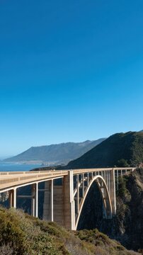 A stunning bridge spans a scenic coastal landscape with clear blue skies and distant mountains