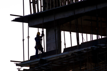 Naklejka premium Construction site, silhouettes of construction industry workers on scaffolding against the sunset light. Constructing and building industry in Brazil