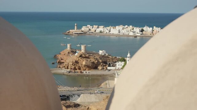 Slow Motion View of Sur Through Lookout Tower Buttresses, Cinematic Framed Panorama of Omani Coastal City