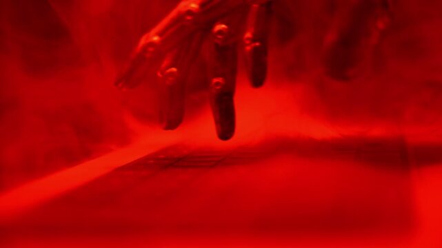 Dramatic red glow highlights a robotic arm. Blurred keyboard sits in the foreground. Smoke swirls around the scene. Precision suggests advanced automation