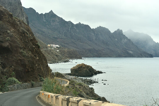 Coastal road winding through rugged volcanic mountains and steep cliffs overlooking the Atlantic Ocean in Anaga Rural Park near Taganana, Tenerife, Canary Islands, Spain