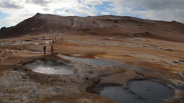 Tourists exploring bubbling mud pots at Hverir geothermal area, Iceland