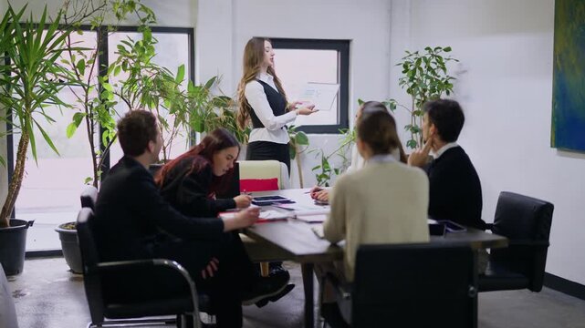 Young business professionals engage in a productive meeting, collaborating on new strategies. They discuss ideas and review presentation charts within a modern office setting.