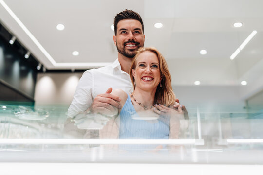 A smiling man and woman browse luxury jewelry at a boutique showcase.