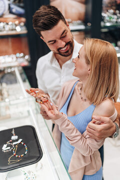 A smiling couple looks at an elegant bracelet while shopping in a luxury jewelry store boutique.