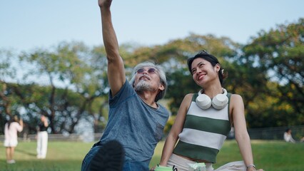 Obraz premium Senior man pointing at the sky while enjoying a picnic with a young woman in a vibrant park