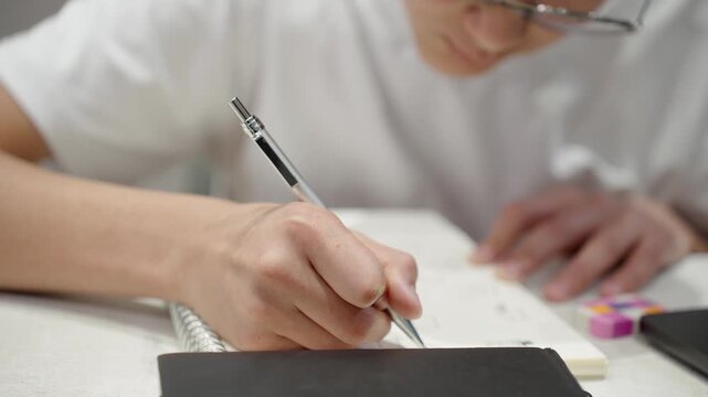 Close up of student writing notes with pen. Learning process, education and concentration concept. Schoolboy making home assignments at home.