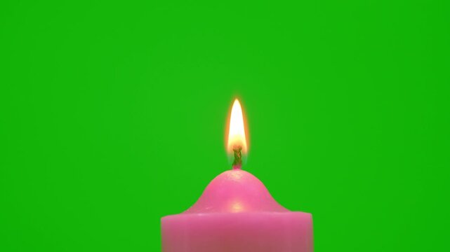 Pink candle with a bright flickering flame stands against a vivid green background, creating a simple contrast scene with warm light, minimal composition, and clean studio style.