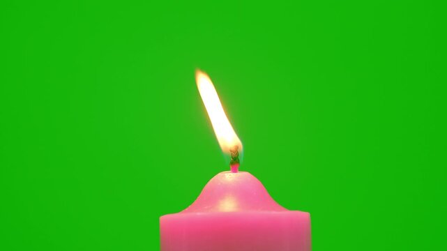 Pink candle with a bright flickering flame stands against a vivid green background, creating a simple contrast scene with warm light, minimal composition, and clean studio style.