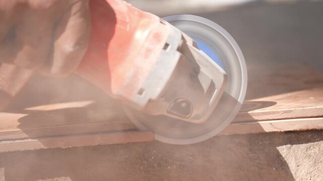 Close-up of a hand using an angle grinder to cut metal, sparks blurred in warm light, showing power tools, construction work, precision cutting, and industrial craftsmanship.