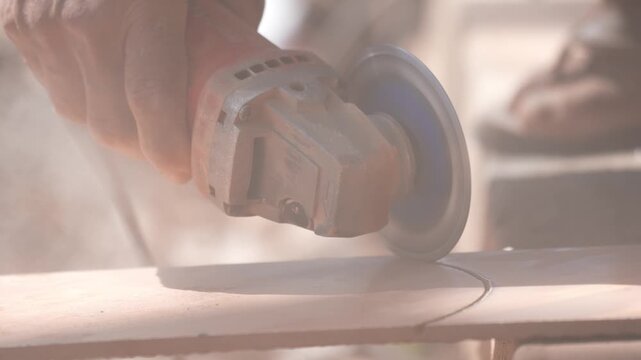 Close-up of a hand using an angle grinder to cut metal, sparks blurred in warm light, showing power tools, construction work, precision cutting, and industrial craftsmanship.
