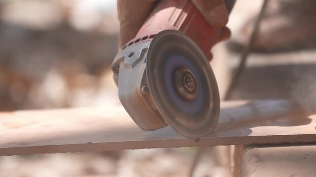 Close-up of a hand using an angle grinder to cut metal, sparks blurred in warm light, showing power tools, construction work, precision cutting, and industrial craftsmanship.