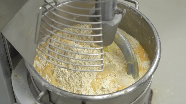 High-angle view of a professional planetary mixer where liquid egg wash is combined with dry flour. This footage captures the essential stage of ingredient mixing in a food factory, perfect for culina