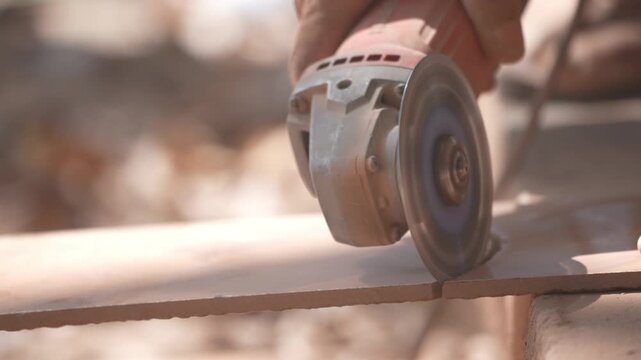 Close-up of a hand using an angle grinder to cut metal, sparks blurred in warm light, showing power tools, construction work, precision cutting, and industrial craftsmanship.