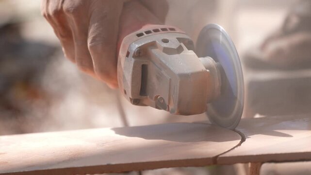 Close-up of a hand using an angle grinder to cut metal, sparks blurred in warm light, showing power tools, construction work, precision cutting, and industrial craftsmanship.
