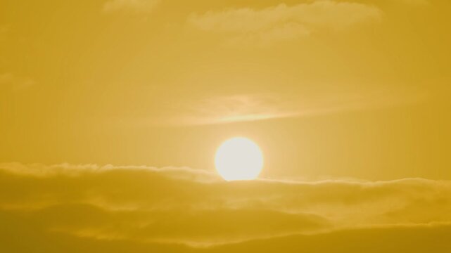 Timelape orange sun hangs low in a hazy sky, surrounded by warm amber tones and soft mist, creating a calm minimalist sunset scene with muted gradients and tranquil mood.