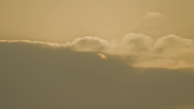 Timelape orange sun hangs low in a hazy sky, surrounded by warm amber tones and soft mist, creating a calm minimalist sunset scene with muted gradients and tranquil mood.