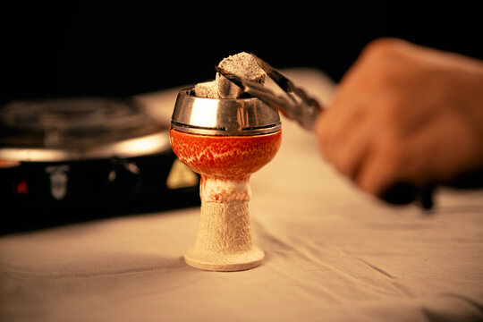 Colocando carb&oacute;n caliente en una cazoleta de shisha con pinzas.