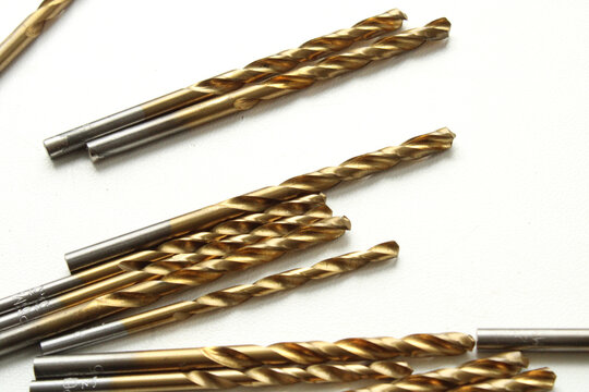 Golden titanium-coated drill bits scattered on a clean white background, showcasing industrial metalwork tools in a high-angle studio shot.