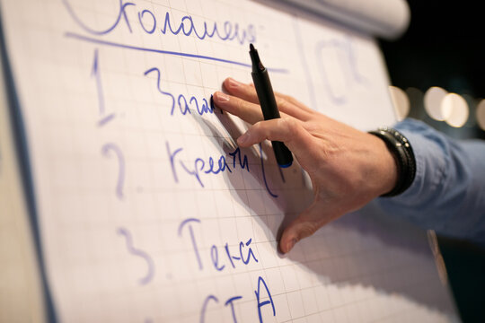 Close-up of a person writing numbers on a flipchart with a black marker