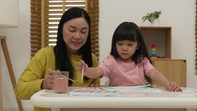 happy mother and preschool child girl painting on paper with watercolor in pan at home