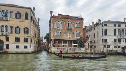 Obraz premium A traditional black gondola with tourists passing historic Venetian palaces along the Grand Canal in Venice