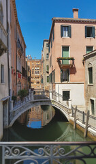 Naklejka premium Scenic view of a small arched stone bridge crossing a narrow canal with historic Venetian houses