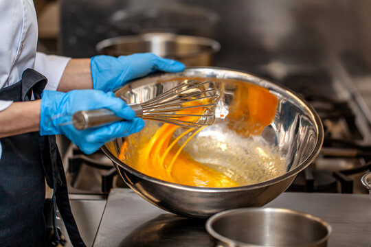 Chef whisking egg mixture in metal bowl kitchen