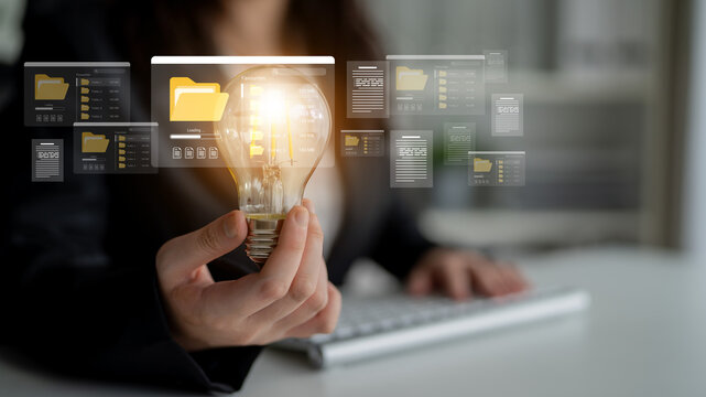 A business professional holds a light bulb symbolizing innovative ideas amidst digital documents and folders in an office setting, emphasizing creativity and information management. Ledger