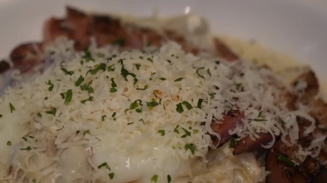 A close-up shot of a classic Italian pasta dish, Spaghetti Carbonara, served in a white bowl. The pasta is coated in a rich, velvety egg and cheese sauce, topped with a mountain of finely shredded Pec