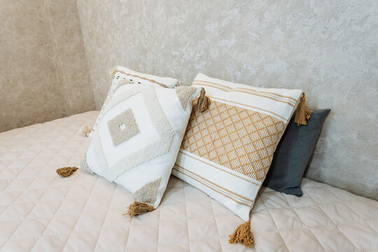 Elegant Bed With Textured Accents. Soft Quilted Coverlet Complemented By Textured Wall Features. Tranquil Morning Scene Featuring Bed Adorned With Tassel Pillows And Textured Backdrop