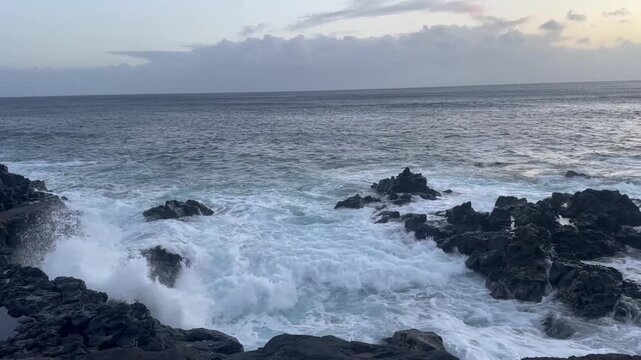 Rocky azores coastline with powerful ocean waves crashing between dark volcanic rocks under cloudy evening sky