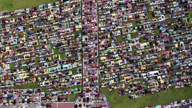 Aerial view of a large crowd of people sitting on colorful prayer mats in organized rows on a green field during a mass prayer event in Klaten, Jawa Tengah, Indonesia.