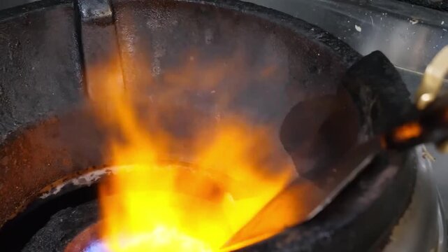 A high-intensity, cinematic close-up shot capturing a glowing piece of metal being heated within a industrial forge. The frame is filled with vibrant orange and yellow flames as the blacksmith prepare