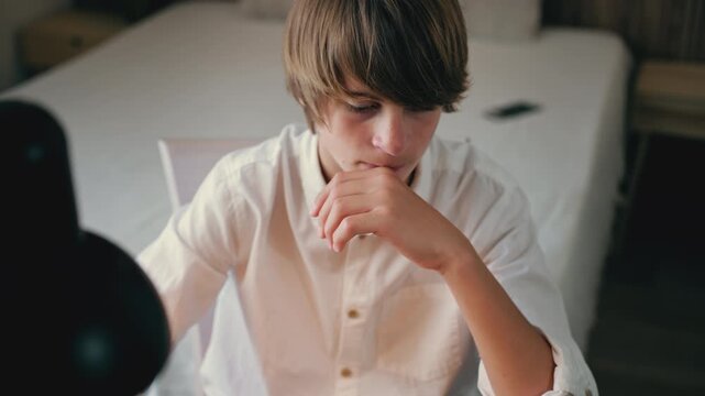High angle view of pensive teen boy study at desk in bedroom, deeply concentrated on schoolwork under warm glow of desk lamp, show moment of deep thought.Education at home, digital learning concept