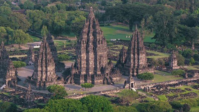 Aerial view of Prambanan Temple complex with its ancient stone spires and lush green parkland with people walking through the grounds in Kecamatan Prambanan, Daerah Istimewa Yogya, Indonesia.