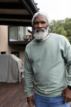 Senior African American man standing on wooden deck near covered grill checking wristwatch