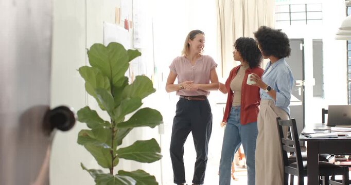 Diverse coworkers entering frame, walking and chatting in office, holding mug, posing for camera