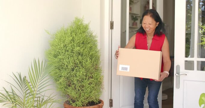 After delivery Senior Asian woman lifting barcode box doorway in red blouse waving to thank driver