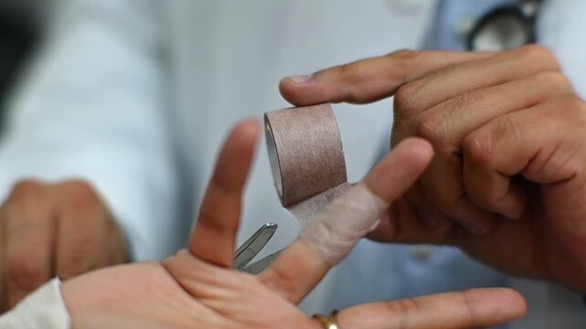 1080p 60fps horizontal video of a doctor treating a finger wound with tape for his patient in his office, both of Latino origin
