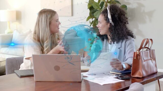 Blonde woman pointing laptop, partner reading papers, working business plan with blue globe overlay
