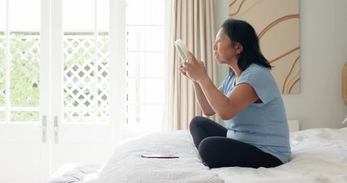 Senior woman seeing white headphones on bed, grabbing, checking fit, using red phone, copy space