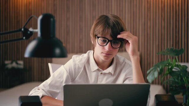 Young student in glasses studying late at night on laptop, feeling fatigue and headache, struggling with difficult task, online learning stress, burnout and mental health concept.