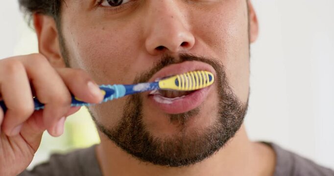 African American man brushing teeth with brush from left, producing white foam to clean in bathroom