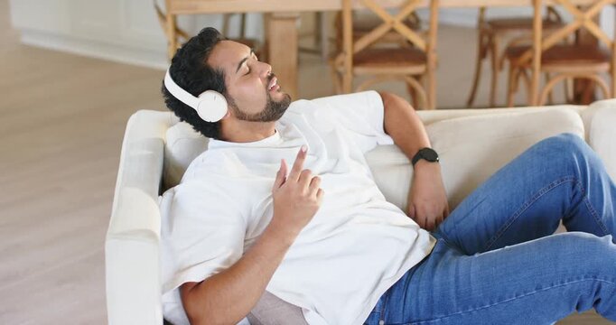 African American man reclining on sofa, music in headphones, mouthing lyrics, sitting up with phone