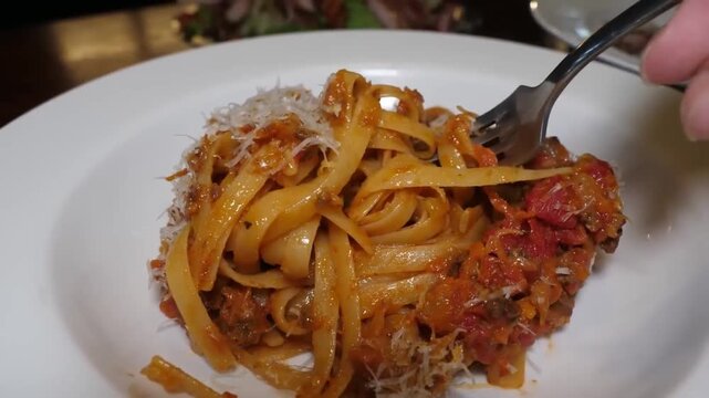 close-up shot of a fork twirling fresh, homemade tagliatelle pasta served with a rich, slow-cooked Bolognese rag&ugrave; sauce and topped with grated parmesan cheese on a white plate. Traditional Italian cui