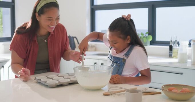 Female parent positioning muffin tin and guiding child ladling batter from glass bowl for baking